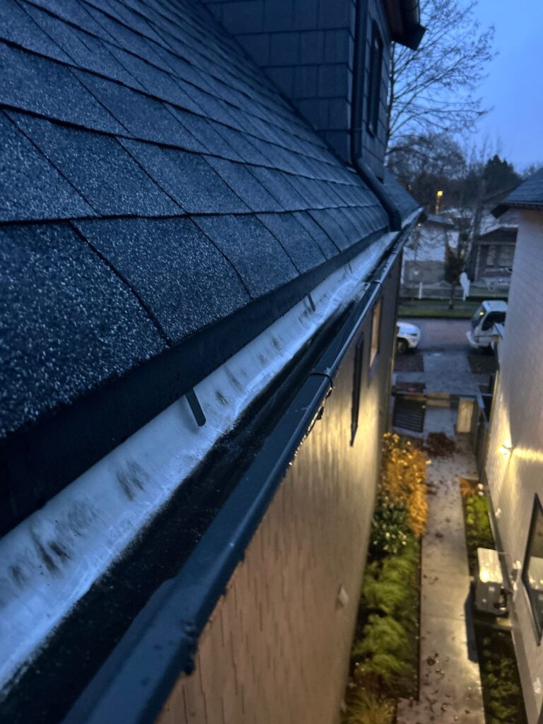 Ice buildup inside residential gutters during winter rain, causing blocked drainage and potential overflow